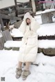 A woman in a white coat is standing in the snow.