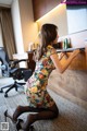 A woman in a floral dress leaning against a desk.