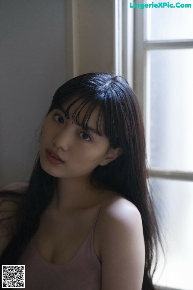 A woman with long black hair sitting in front of a window.