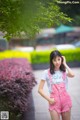 A woman in a white shirt and pink overalls posing for a picture.