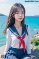 A woman in a sailor outfit sitting on a rock by the ocean.