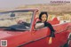 A woman sitting in the driver's seat of a red convertible car.