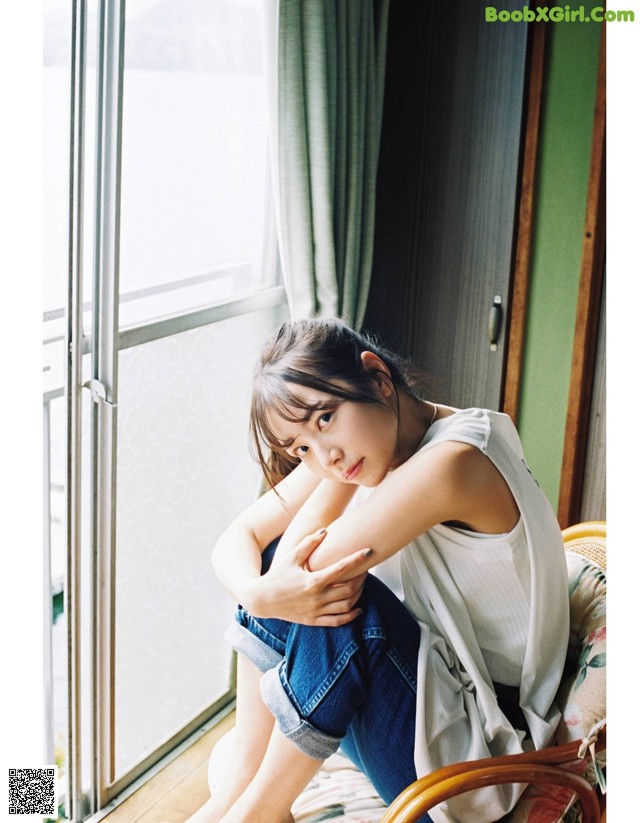 A woman sitting on a chair in front of a window.