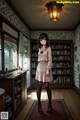 A girl standing in front of a book shelf in a room.