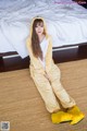 A woman in a yellow pajamas sitting on a bed.