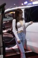 A woman standing next to a white car at a car show.