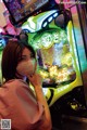 A woman wearing a face mask in front of a slot machine.