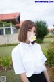 A woman in a white shirt and black skirt holding a white flower.