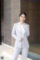 a woman in a white suit standing in front of a wall