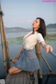 A woman in a white shirt and plaid skirt sitting on a wooden dock.